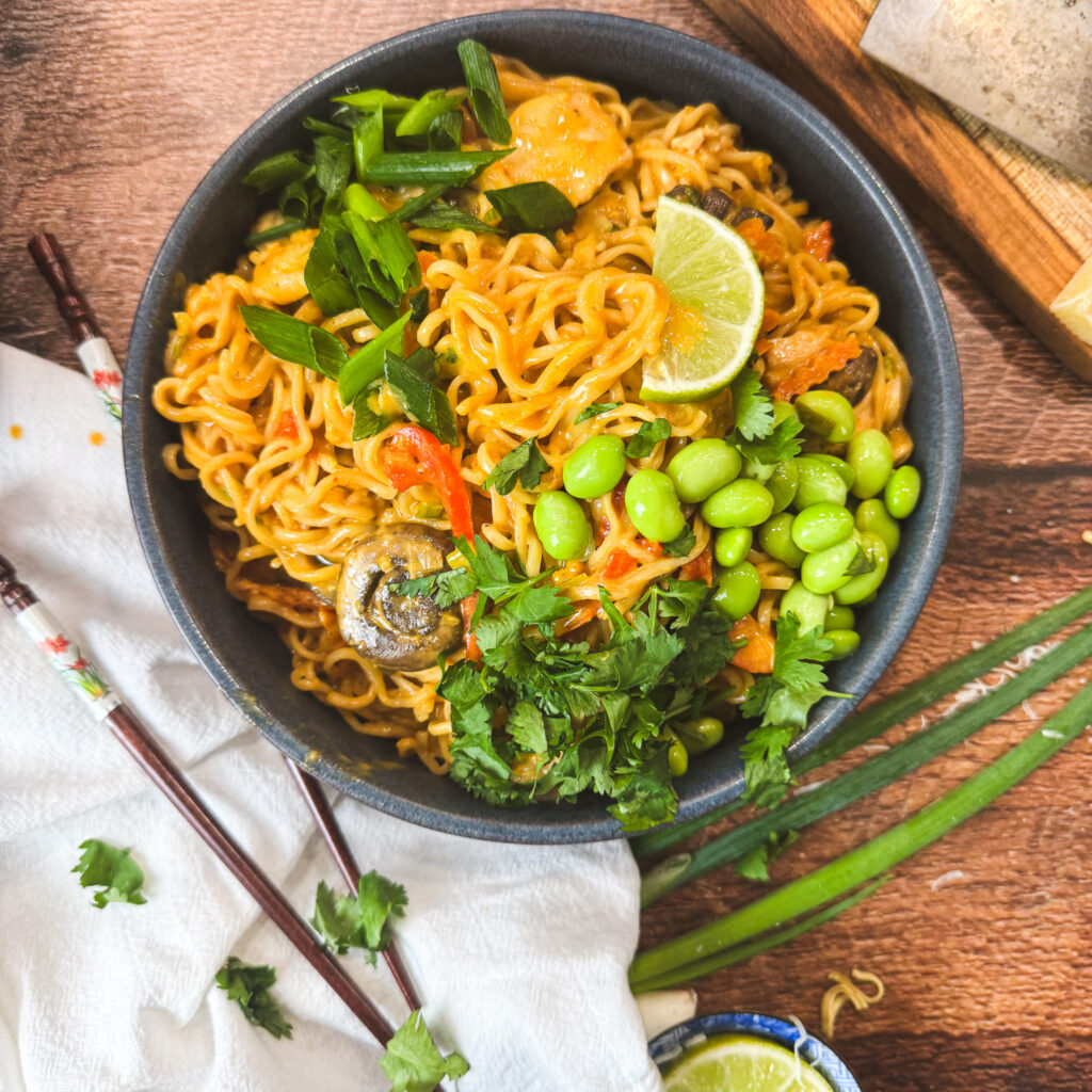 Bright, inviting bowl of curry noodles garnished with cilantro, green onions, and lime slices on a wooden table — ready to dig in.