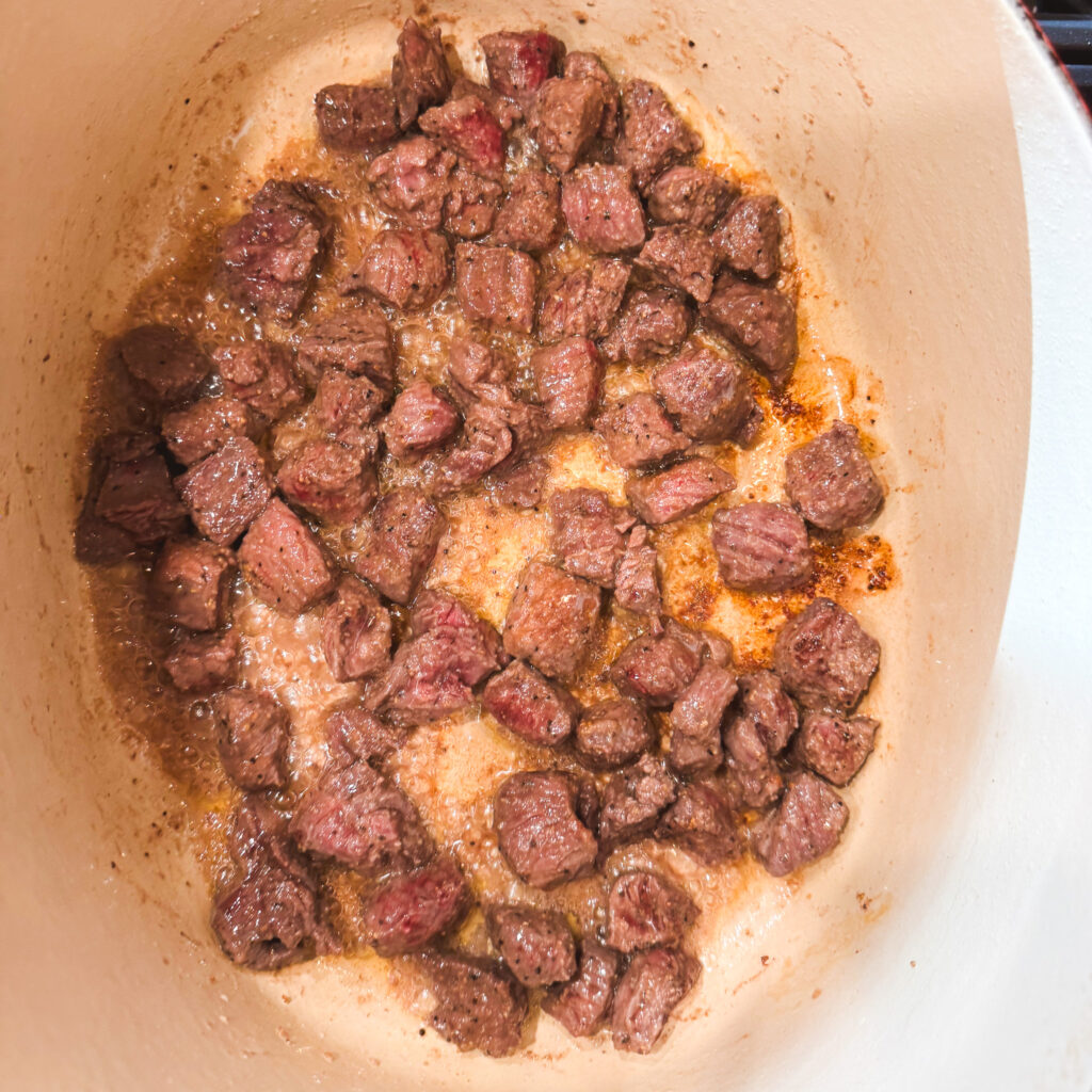 The Dutch oven now filled with browned beef cubes, caramelized on the edges and sitting in bubbling juices. Golden-brown fond clings to the bottom of the pot, ready to flavor the soup.