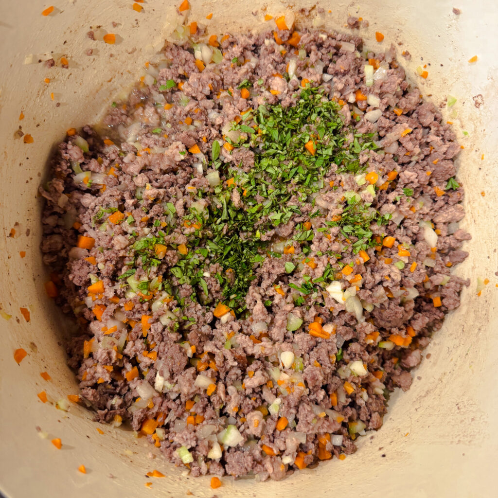 Fresh minced herbs added to the meat and vegetable mixture in a Dutch oven to build flavor for bolognese sauce.