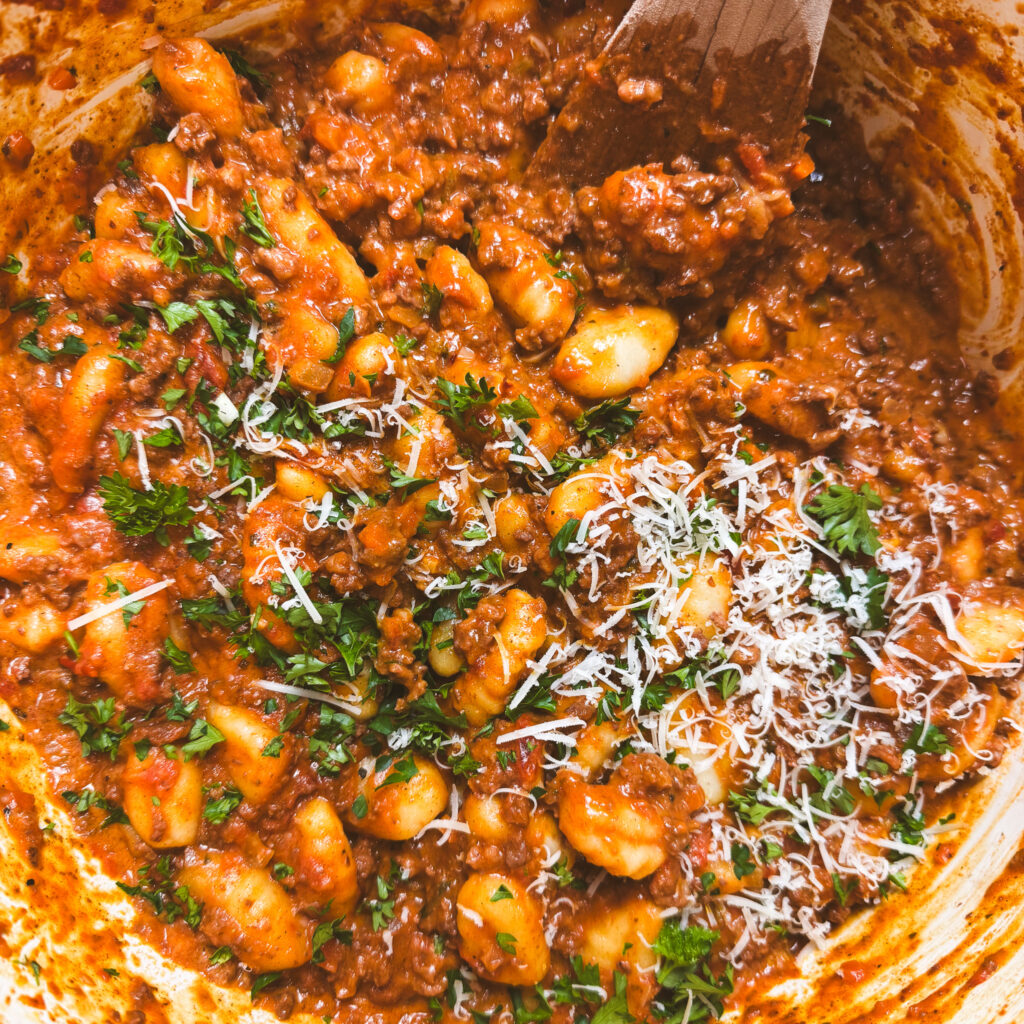 Finished one pot gnocchi bolognese topped with grated parmesan and fresh herbs in a Dutch oven.