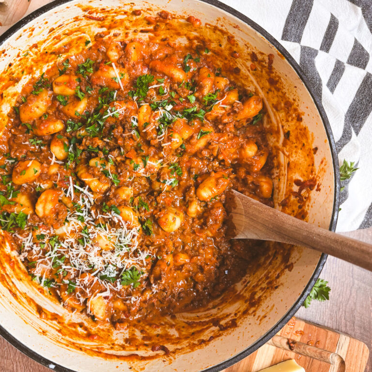 Finished one pot gnocchi bolognese topped with grated parmesan and fresh herbs with a wooden spoon for serving.