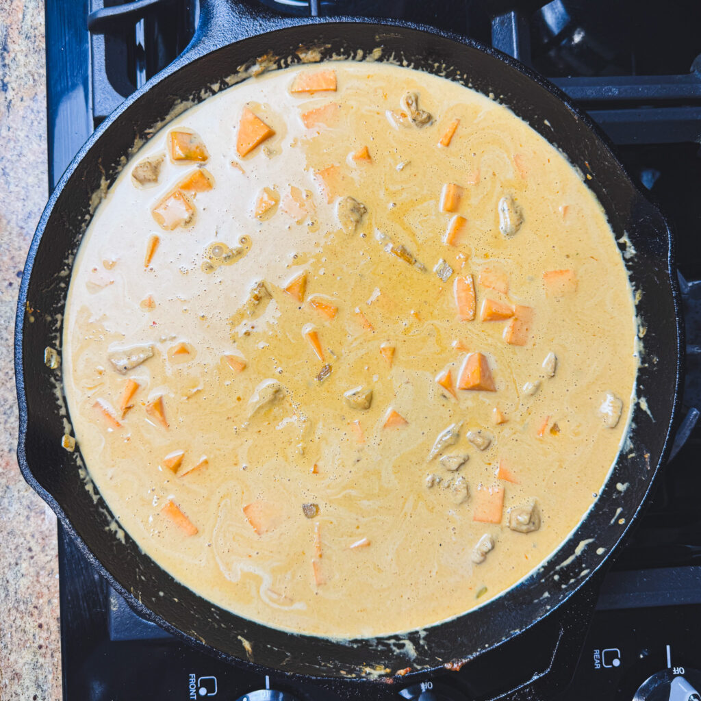 Coconut milk and peanut curry sauce simmering with chicken and sweet potatoes in a cast iron skillet.