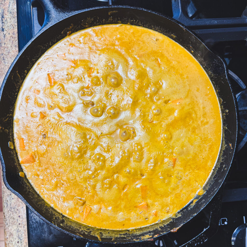 Peanut curry sauce gently bubbling in a cast iron skillet as it thickens.
