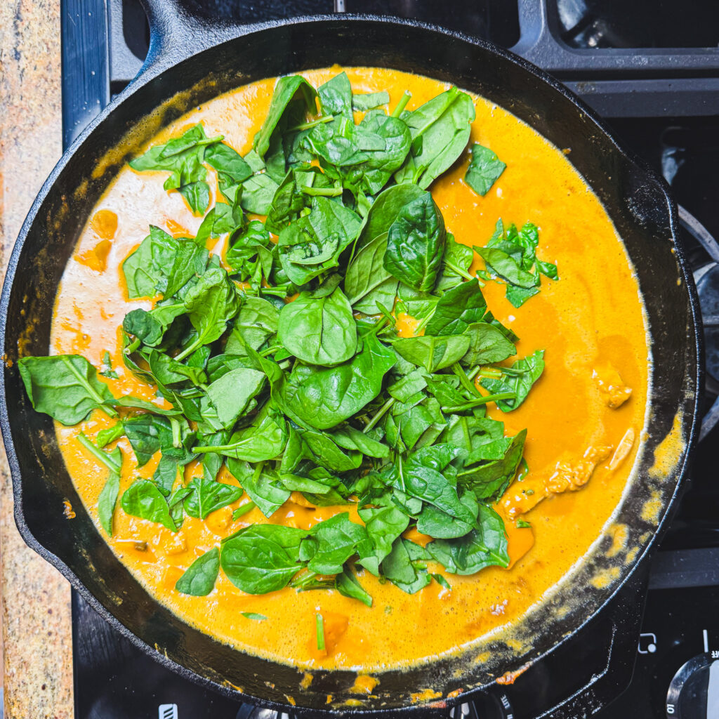 Fresh spinach added to peanut chicken curry in a cast iron skillet.