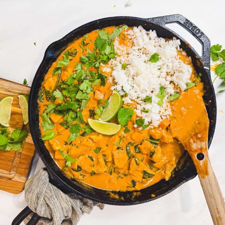 Finished peanut chicken curry served in a cast iron skillet with white rice, fresh cilantro, and lime wedges.