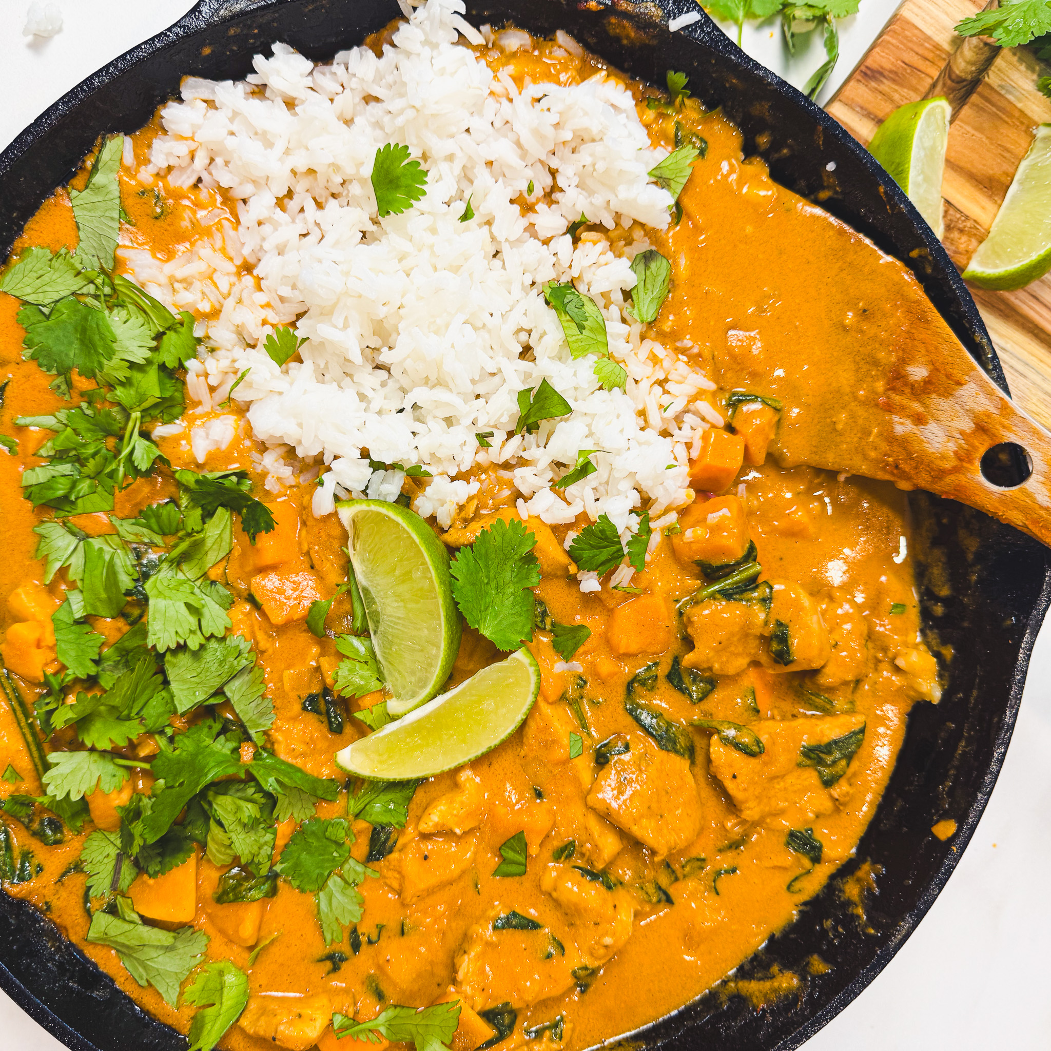 Finished peanut chicken curry served in a cast iron skillet with white rice, fresh cilantro, and lime wedges.
