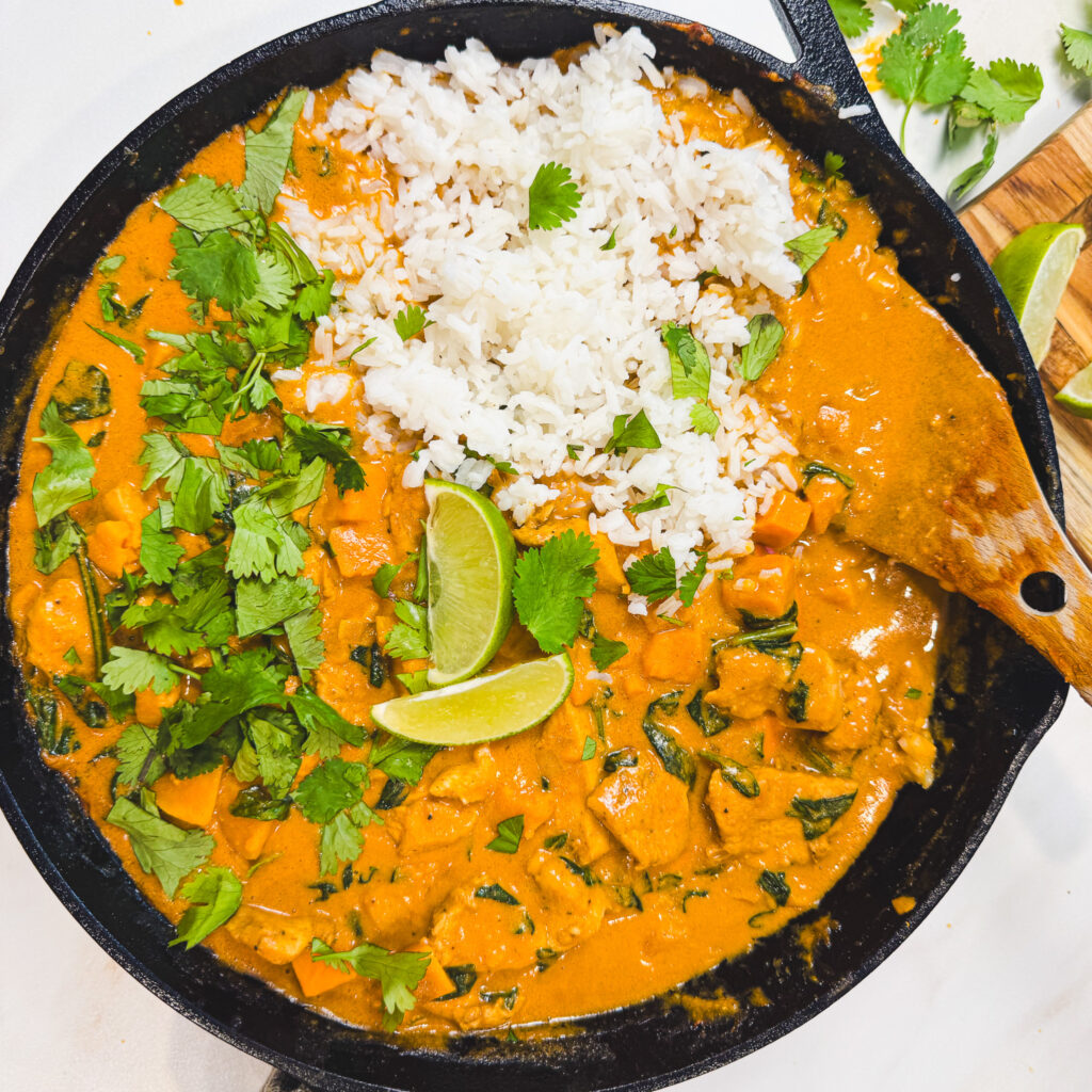 Finished peanut chicken curry served in a cast iron skillet with white rice, fresh cilantro, and lime wedges.