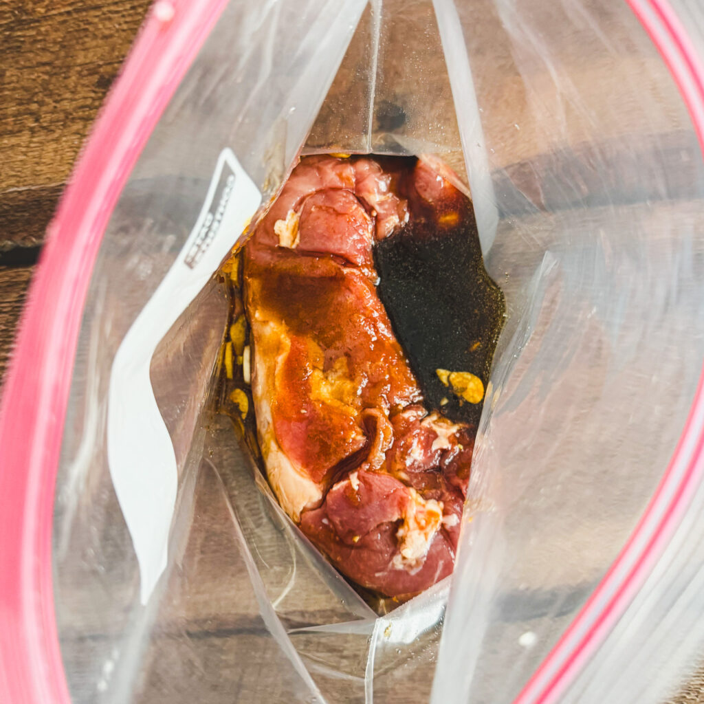 Pork tenderloin marinating in a soy-based marinade inside a zip-top bag, ready to absorb flavor.