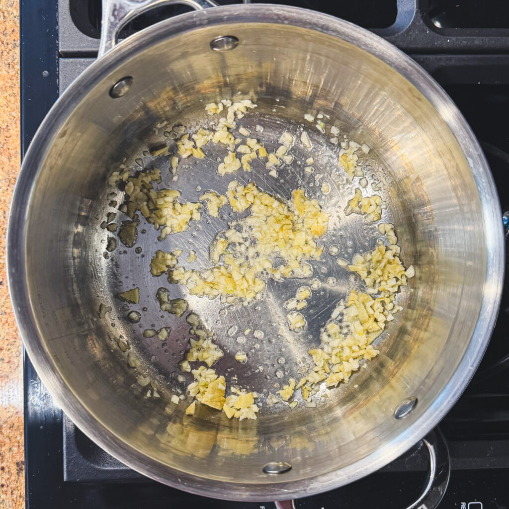 Minced garlic gently sautéing in a stainless steel pot to build the ramen broth base.