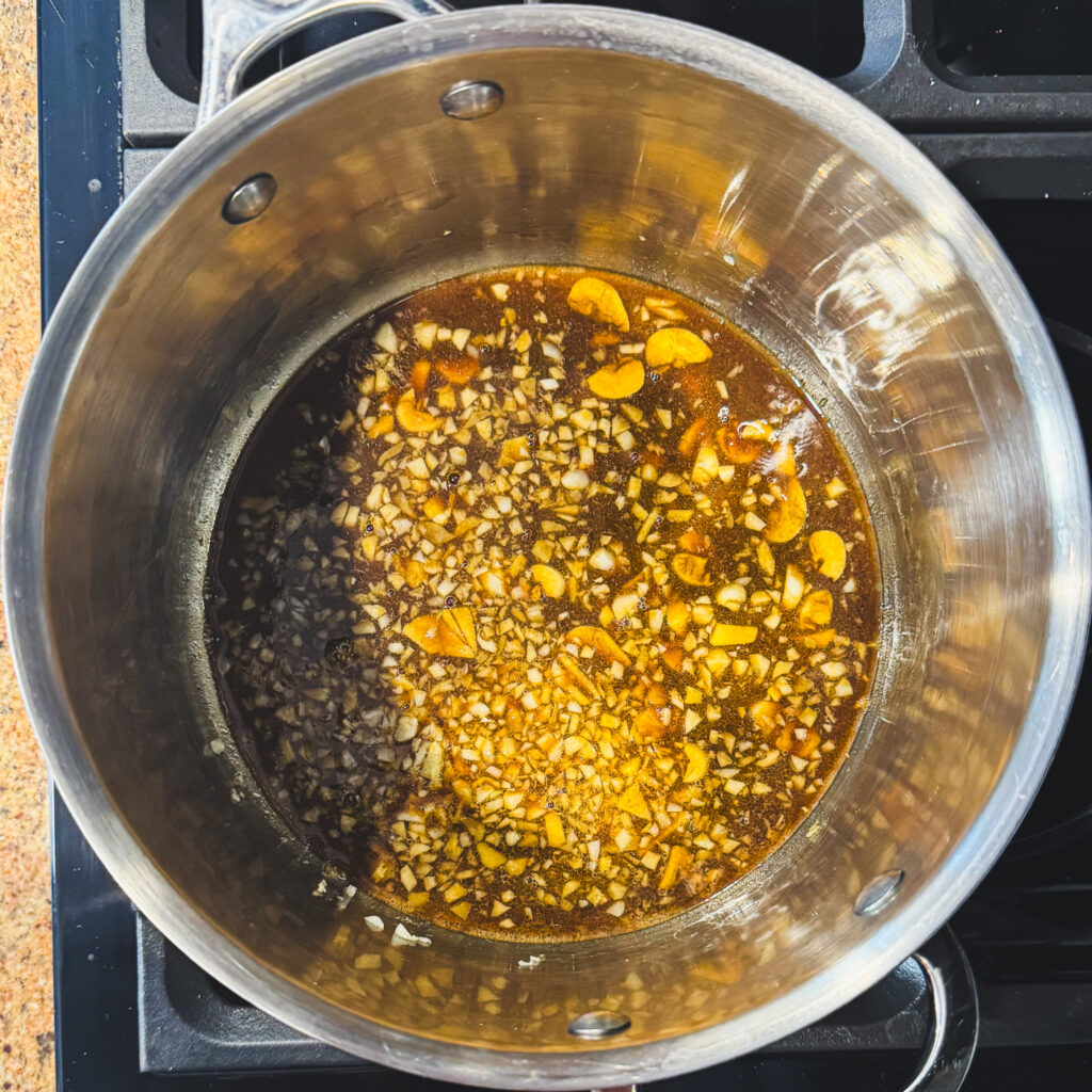 Soy-based pork marinade added to sautéed garlic in a pot, forming the base of the ramen broth.