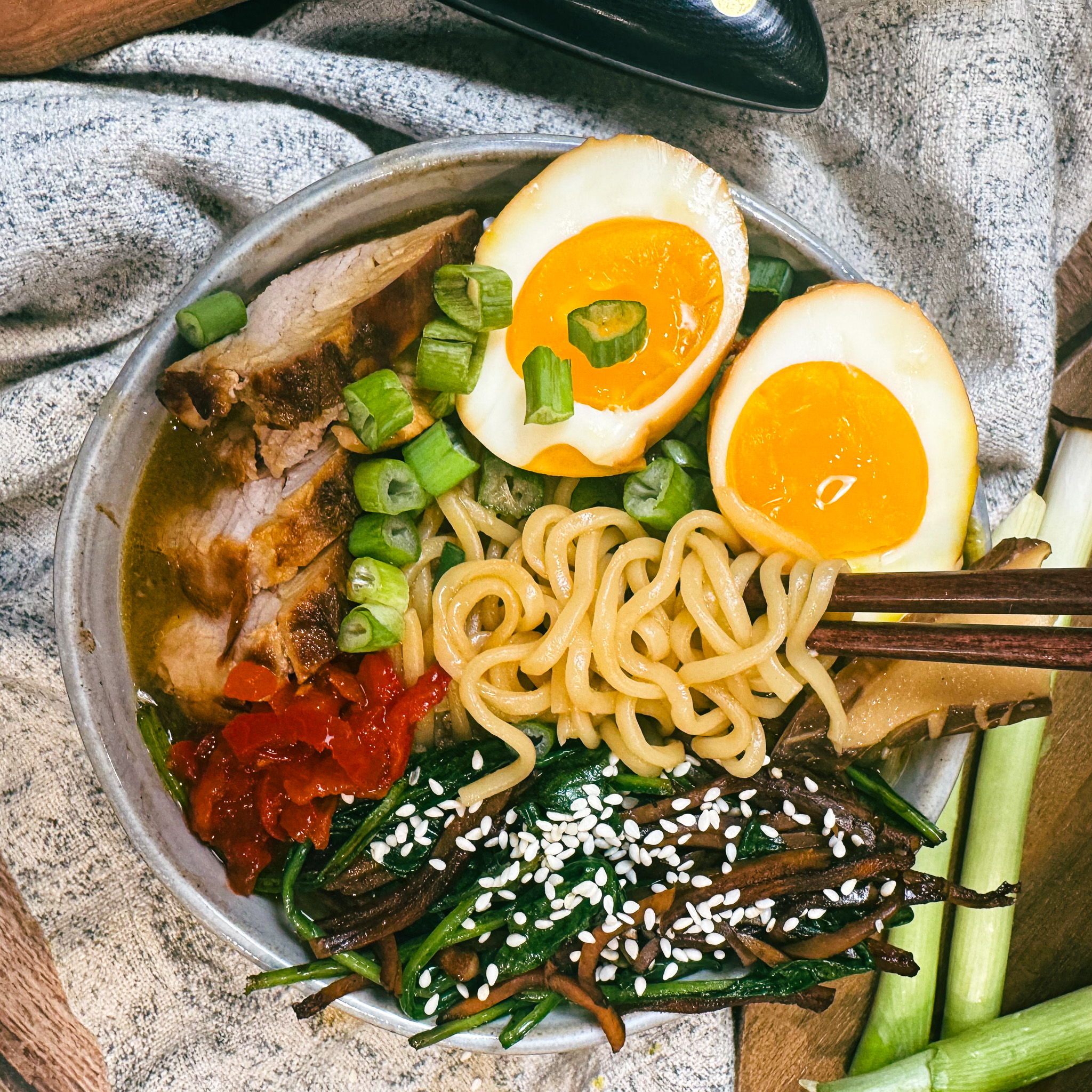 Close-up of ramen noodles with soft-boiled soy eggs, sliced pork tenderloin, scallions, and sesame seeds.