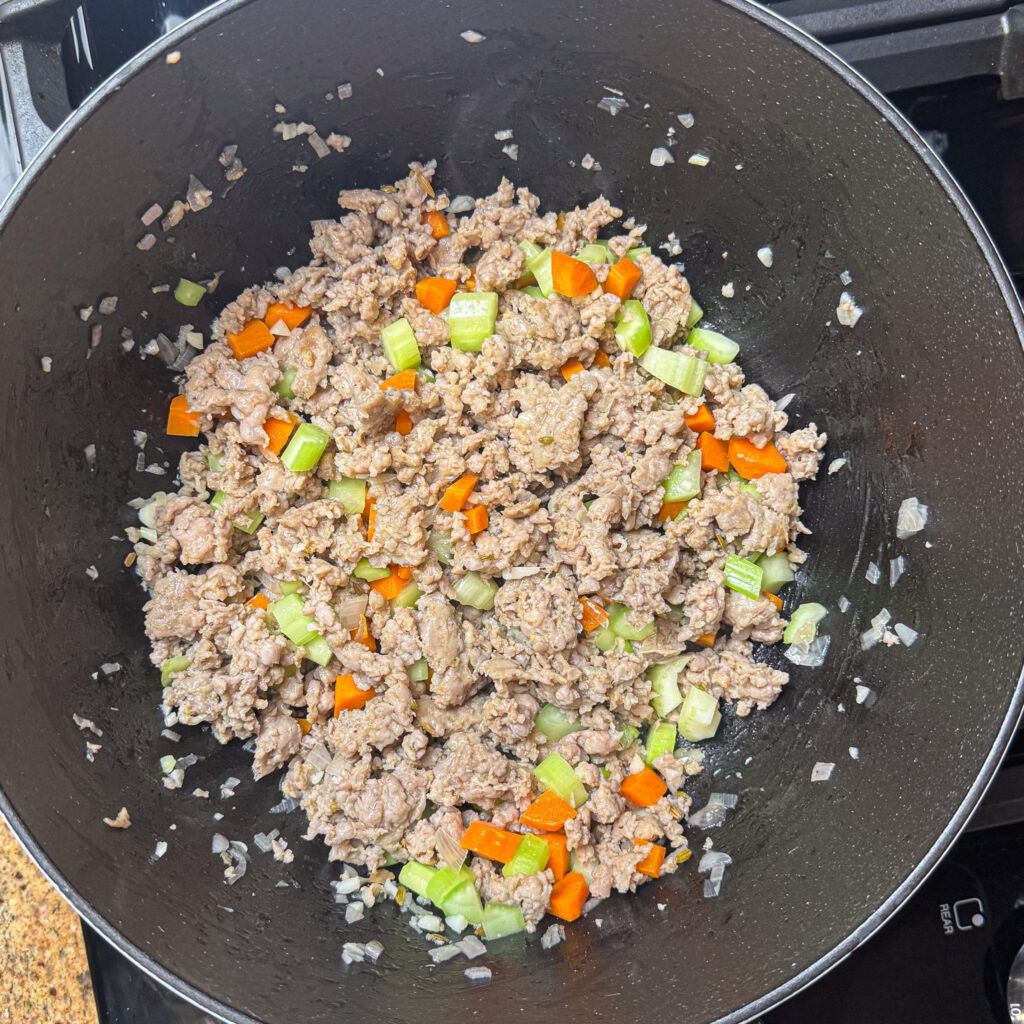 Italian sausage browning in a Dutch oven with diced shallots, the first step in making creamy Tuscan tortellini soup.