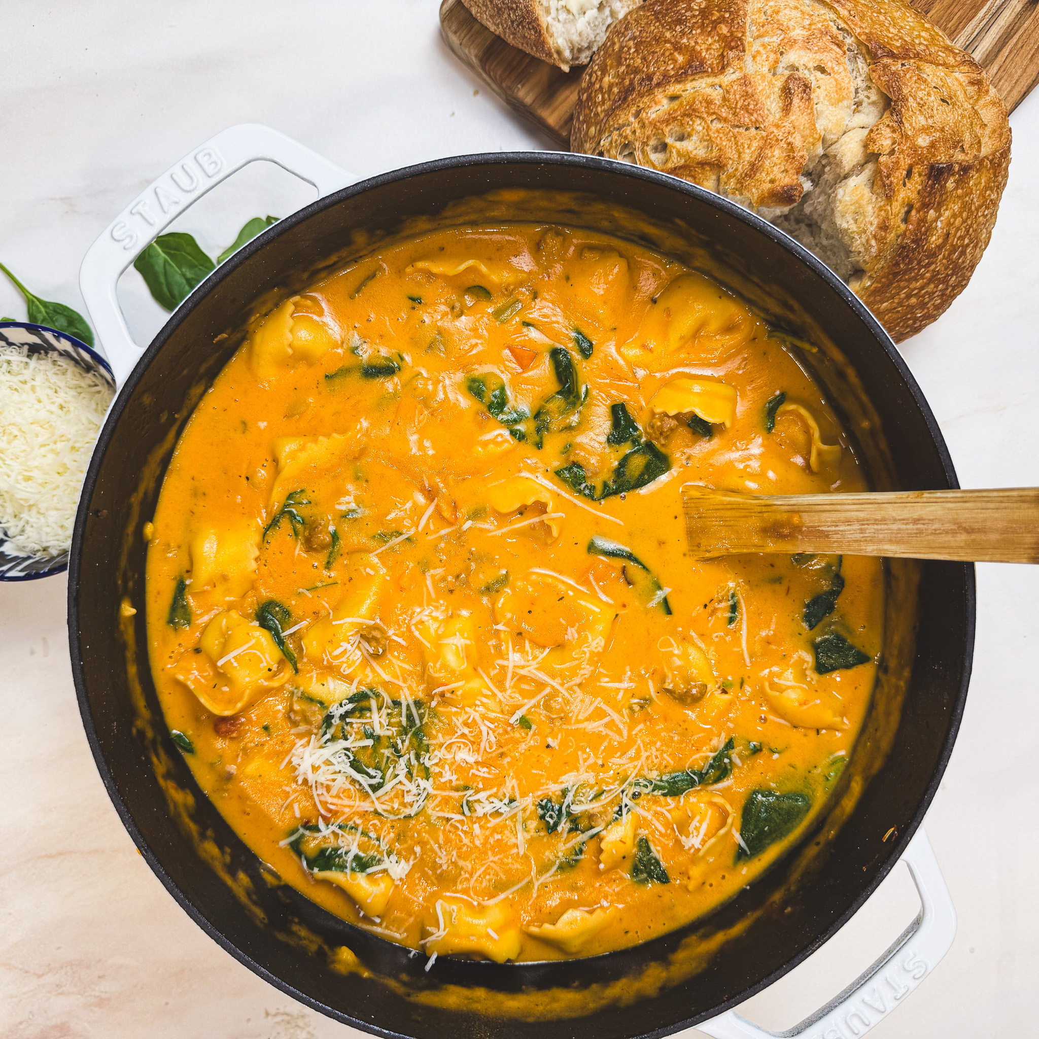 Creamy Tuscan tortellini soup with sausage, spinach, and parmesan cheese in a Dutch oven served with crusty bread.