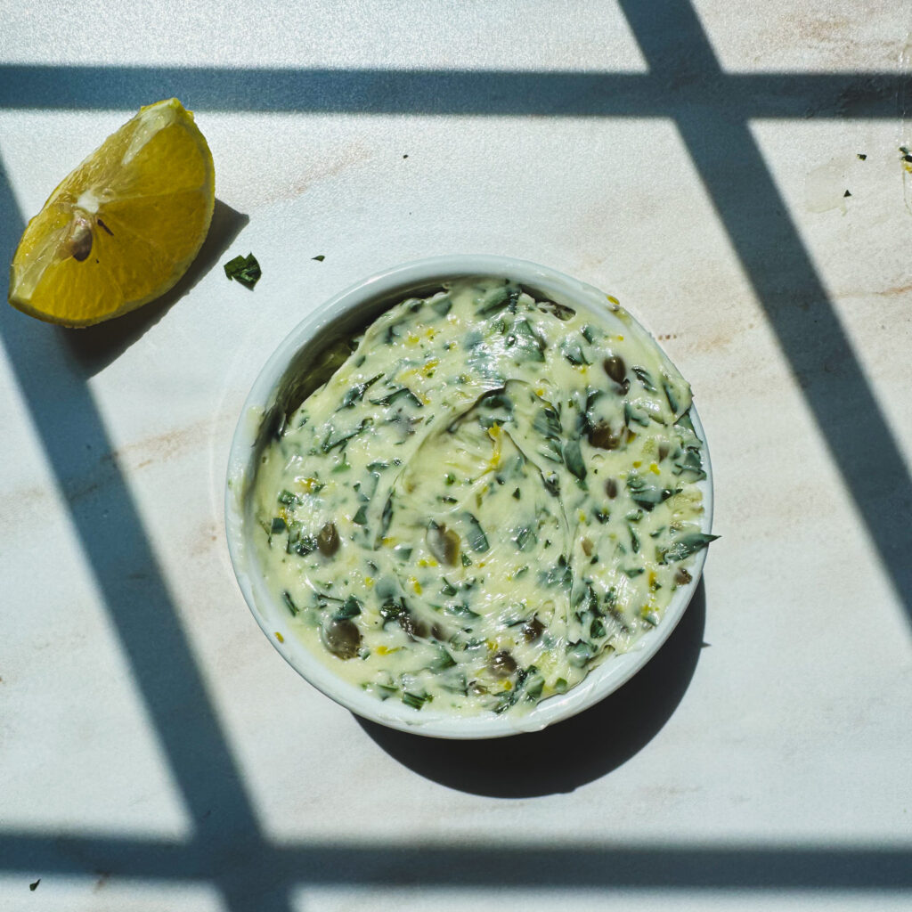 Small white ramekin filled with creamy homemade lemon caper butter beside a fresh lemon wedge.