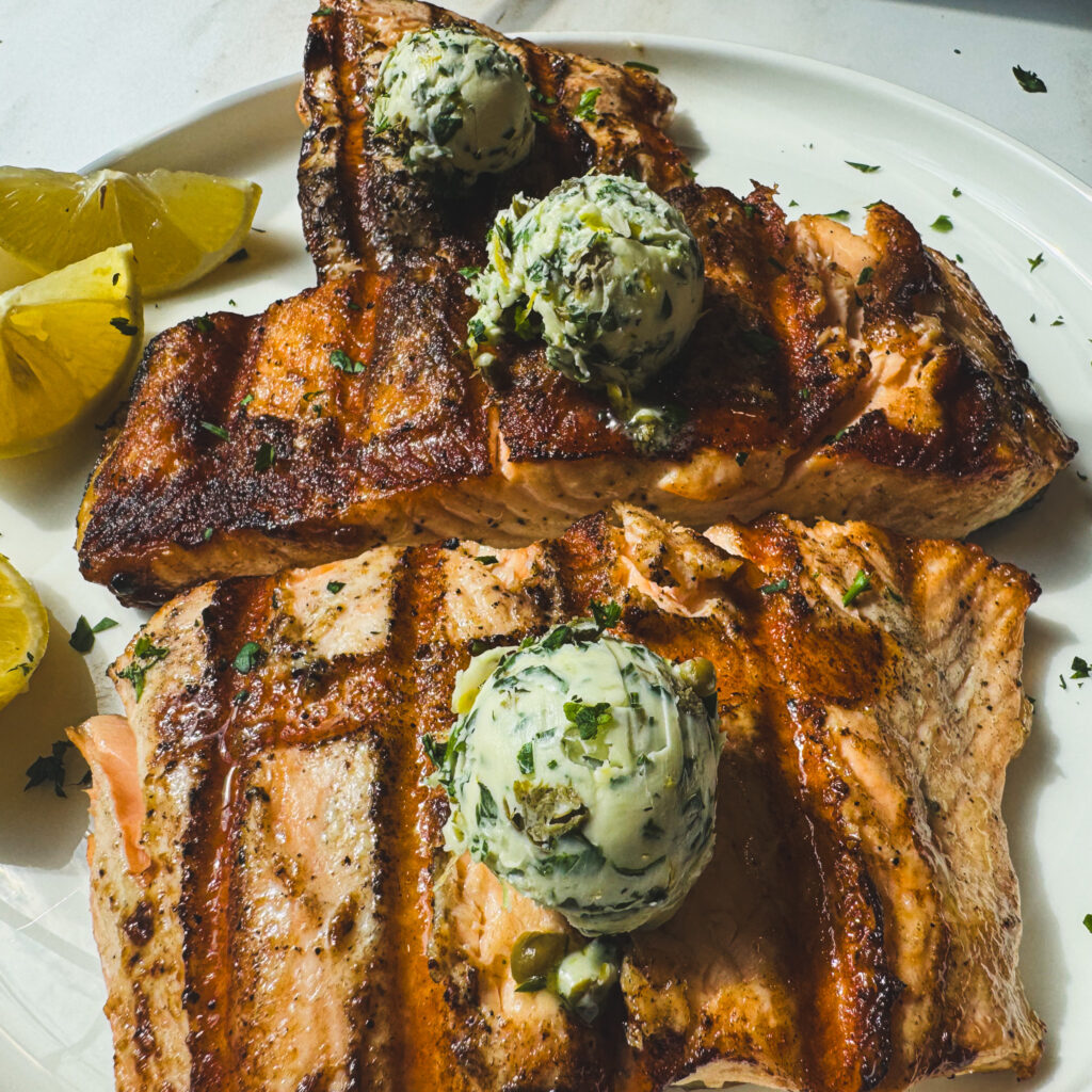 Grilled salmon topped with scoops of homemade lemon caper butter and served with fresh lemon wedges.