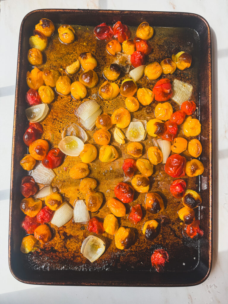 Roasted cherry tomatoes, onion, and garlic caramelized on a baking sheet for homemade roasted tomato pasta sauce.