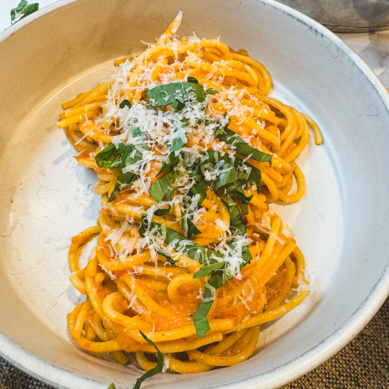 Bowl of roasted tomato pasta topped with grated Parmesan and fresh basil.