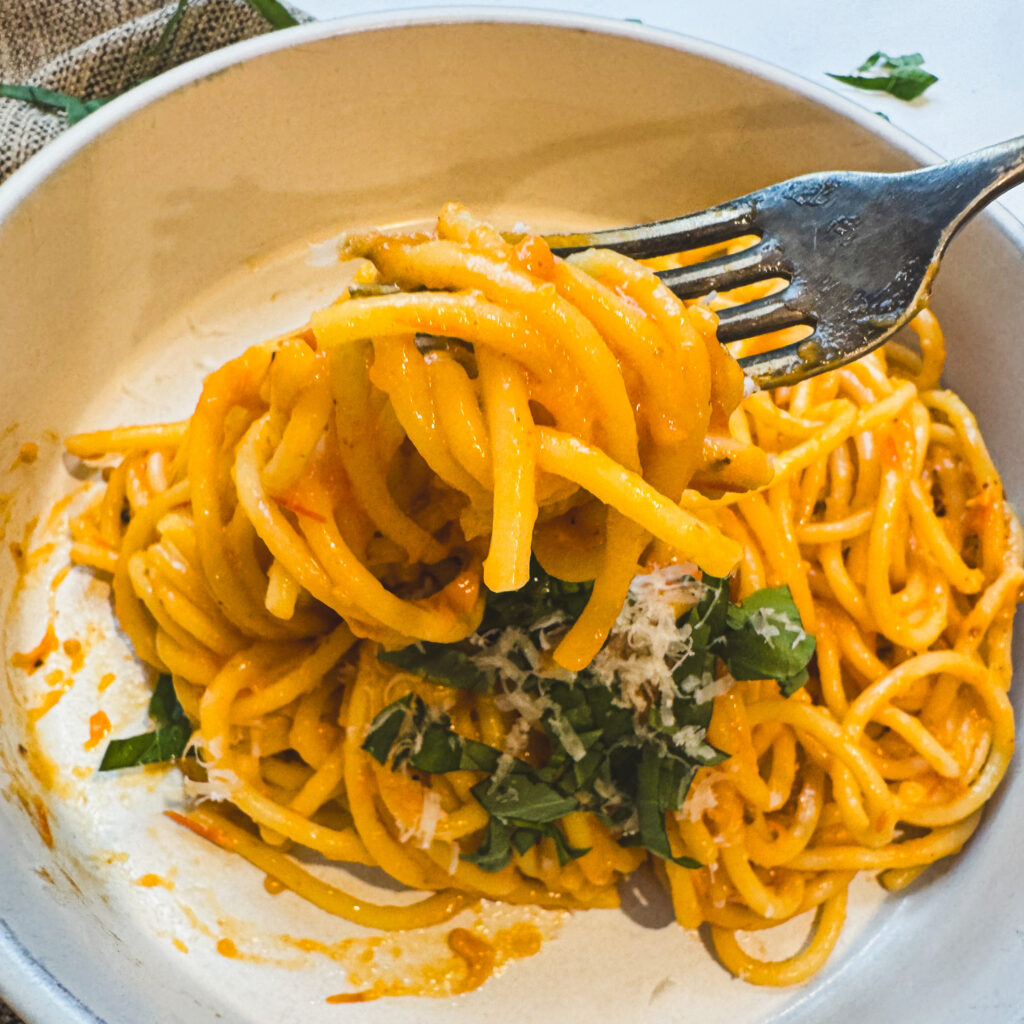 Fork twirling creamy roasted tomato pasta with fresh basil and grated Parmesan.