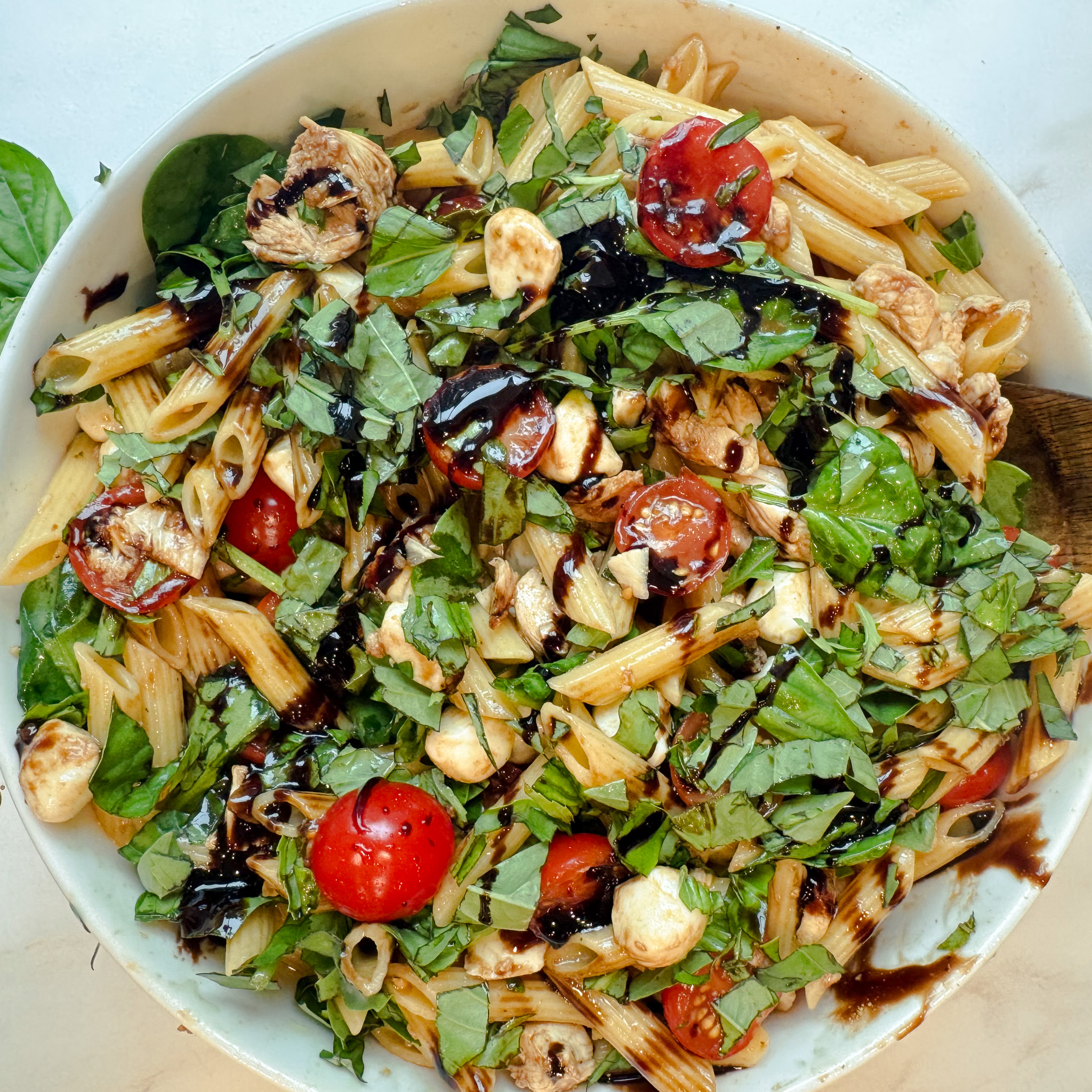 Close-up of grilled chicken Caprese pasta salad with juicy marinated tomatoes, fresh basil, mozzarella pearls, and balsamic glaze.