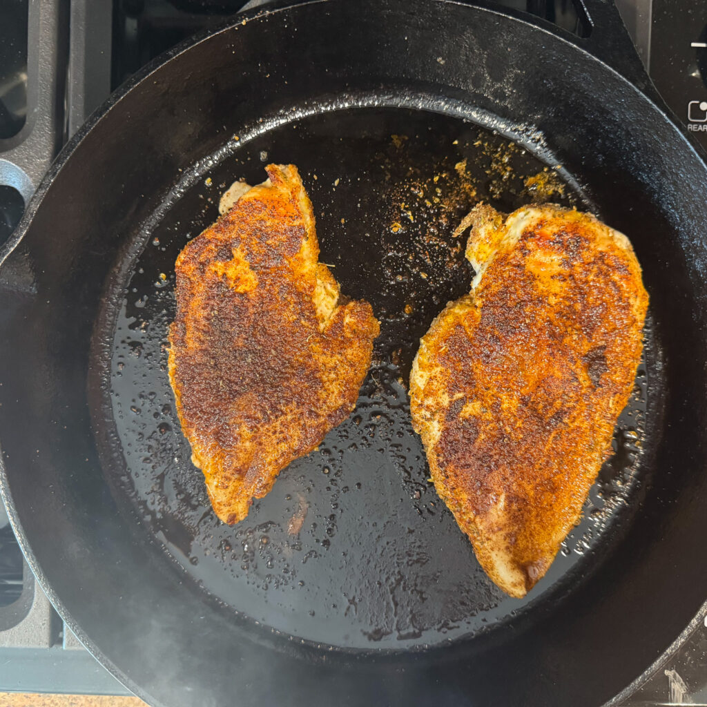 Seasoned chicken breasts seared in a cast iron skillet until deeply golden brown.