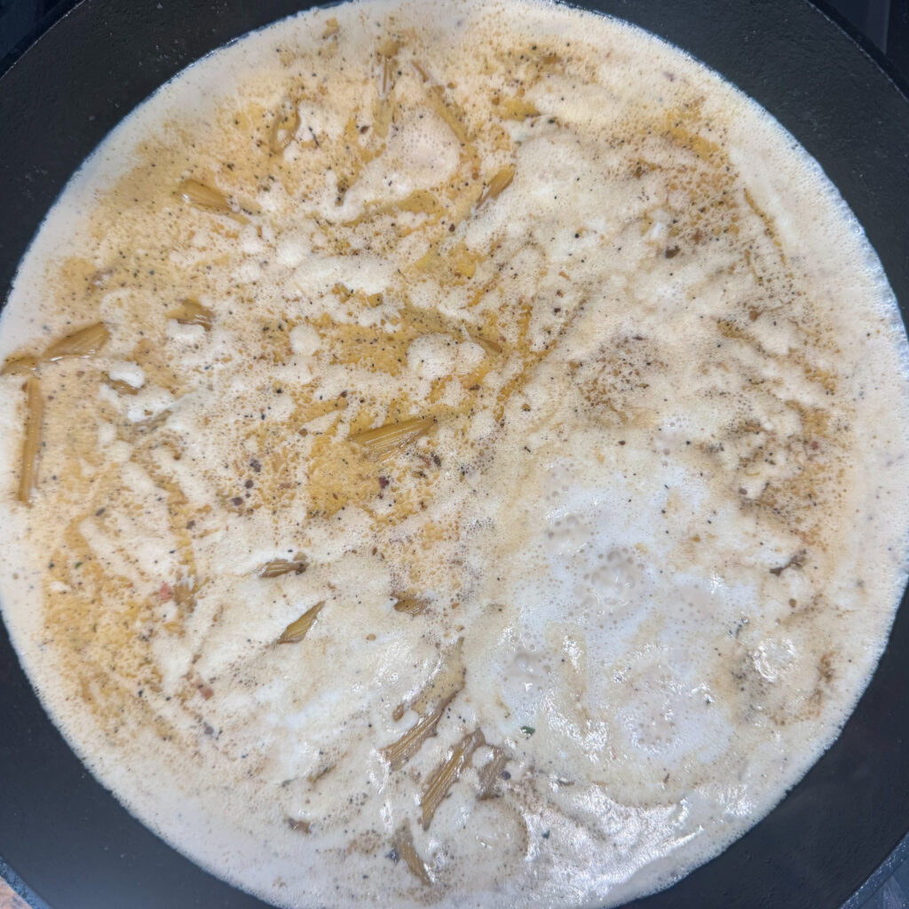 Penne pasta simmering in chicken broth and heavy cream for a one pot creamy pasta sauce.