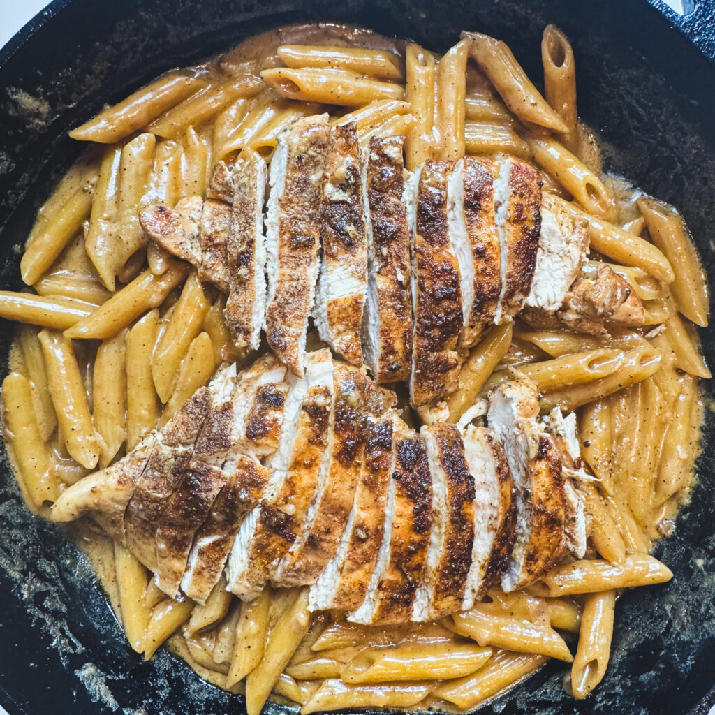 Sliced seared chicken breasts arranged over creamy one pot penne pasta.