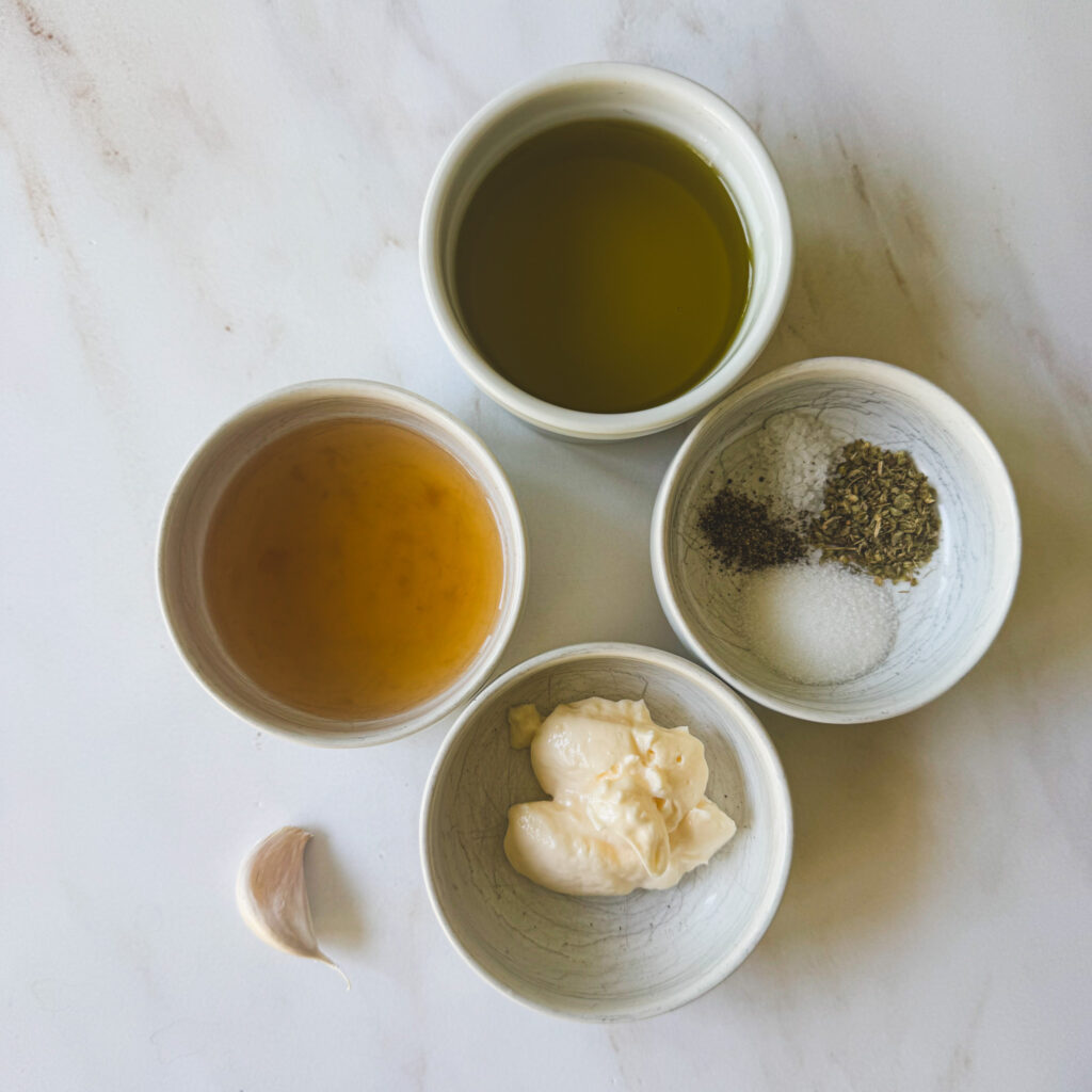 Ingredients for homemade creamy Italian dressing including olive oil, red wine vinegar, mayonnaise, garlic, dried Italian seasoning, salt, and black pepper.