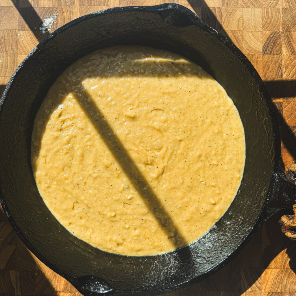 Batter in skillet: Brown butter apple cake batter spread into a cast iron skillet for apple fritter skillet cake.