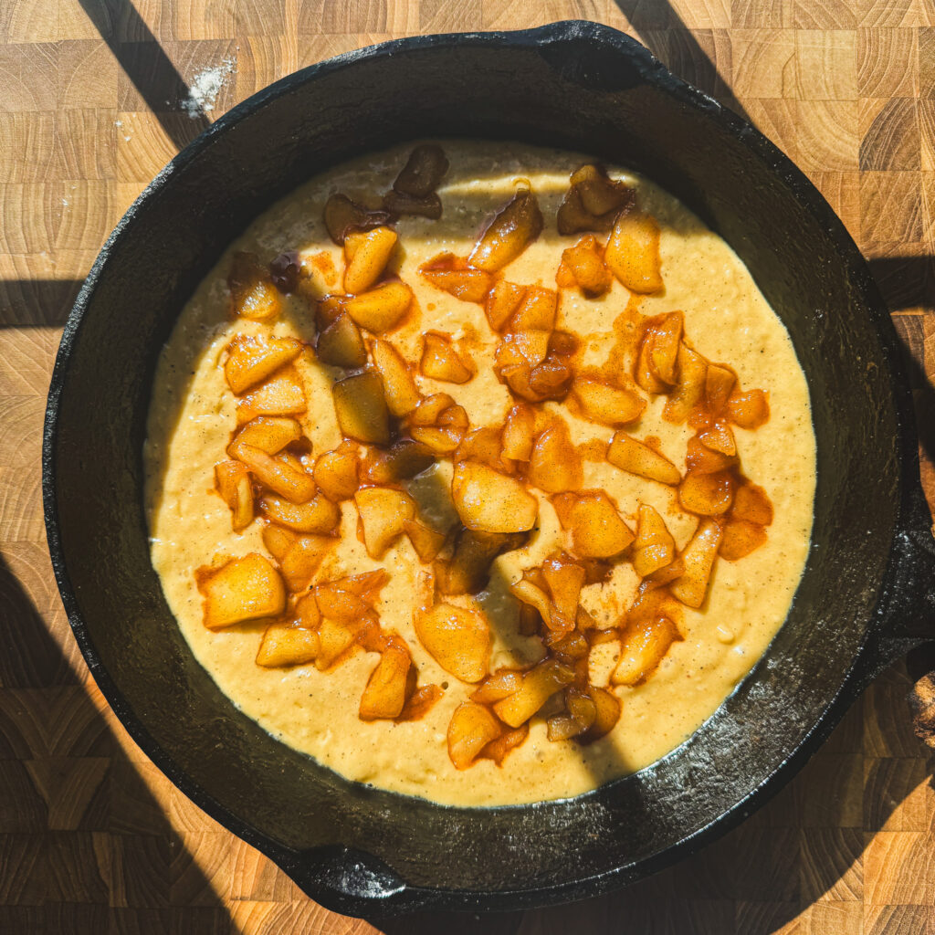 First apple layer: Cinnamon brown sugar apples layered over batter for a gooey apple fritter skillet cake.