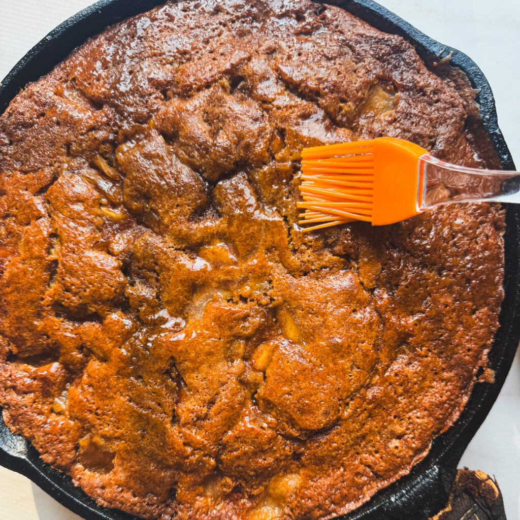 Brushing cake: Brushing warm apple fritter skillet cake with melted butter before adding the sweet vanilla glaze.
