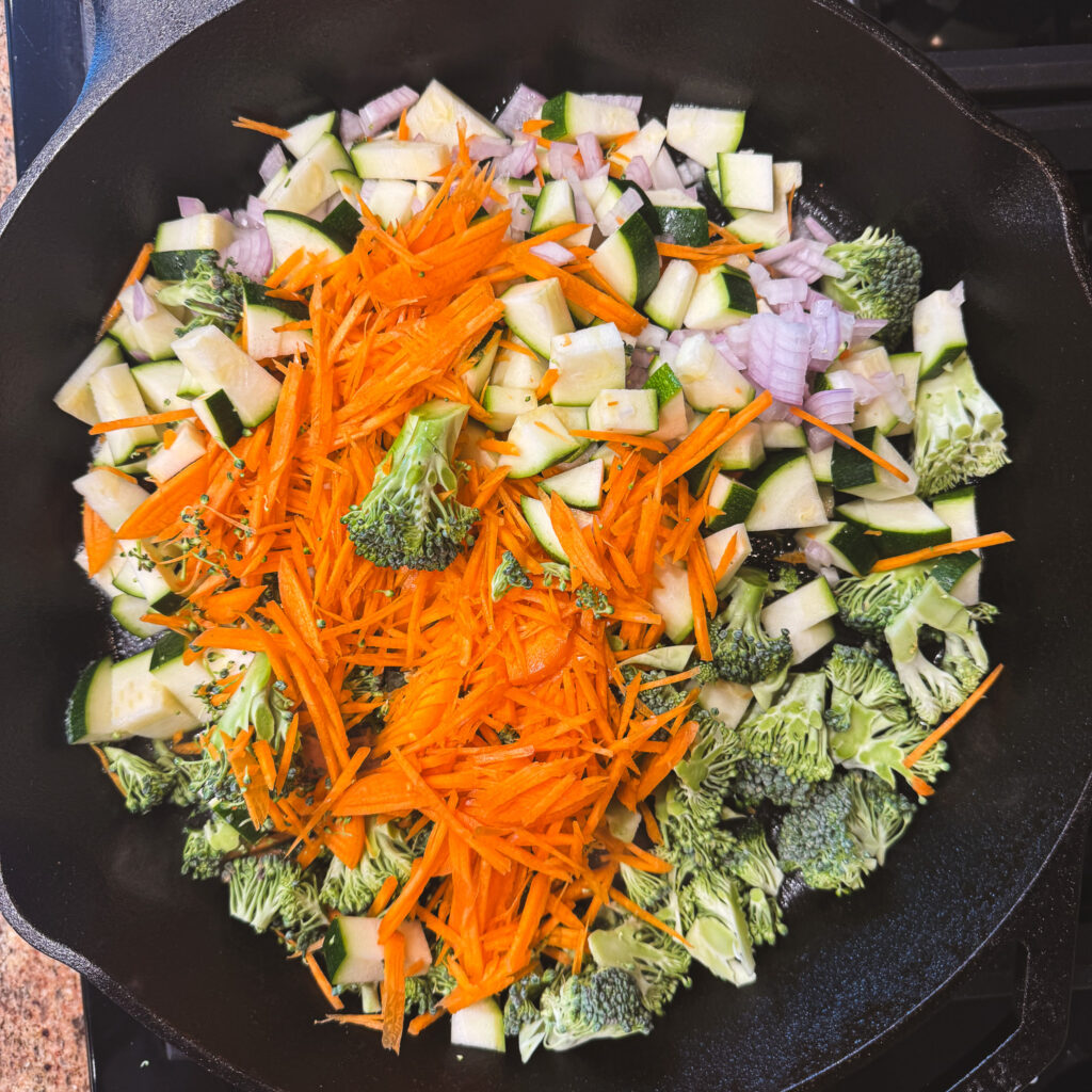 Chopped broccoli, zucchini, carrots and shallot added to a cast iron skillet.