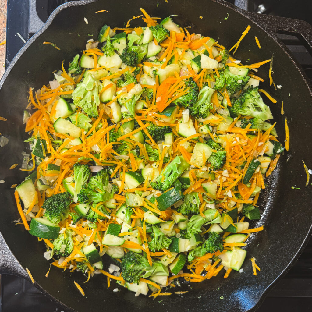 Broccoli, zucchini, carrots and shallot sautéing in a cast iron skillet.