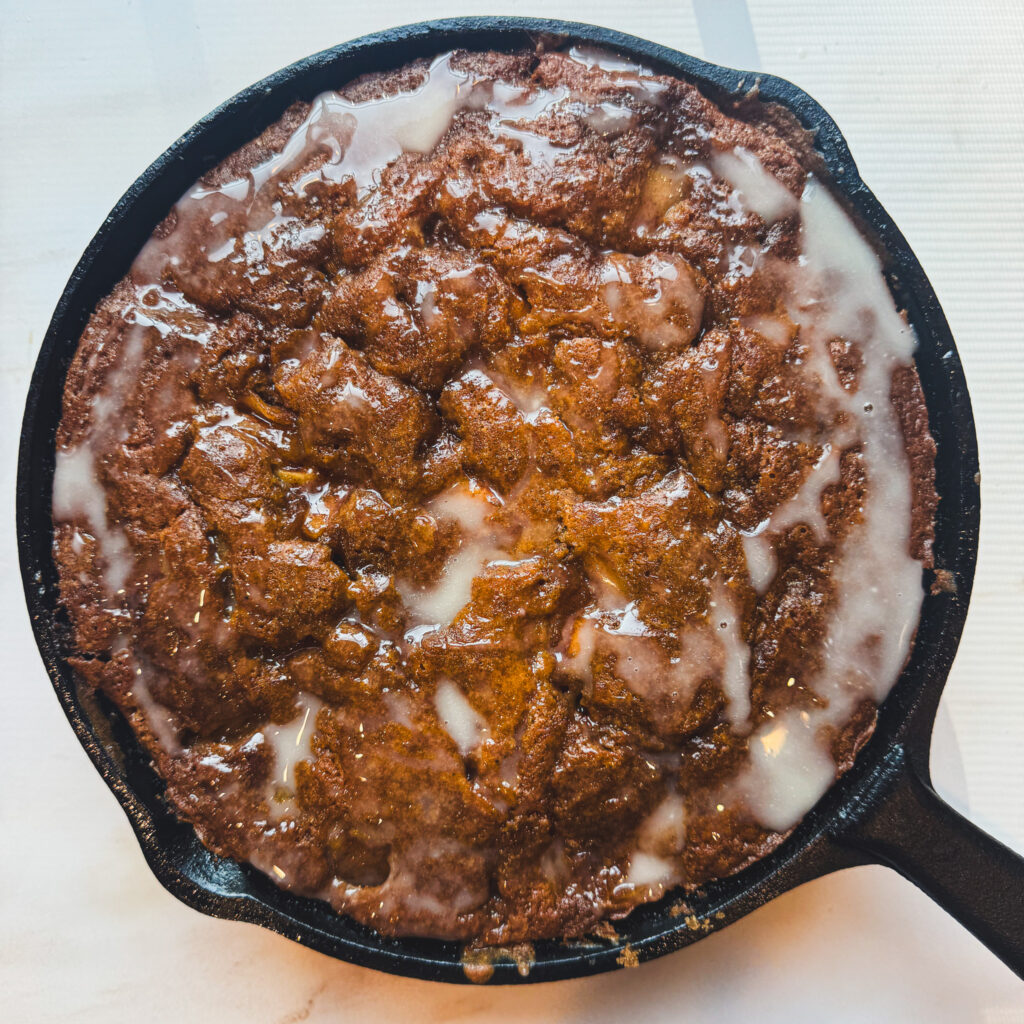 Finished overhead: Glazed apple fritter skillet cake baked in cast iron with cinnamon apples and brown butter.