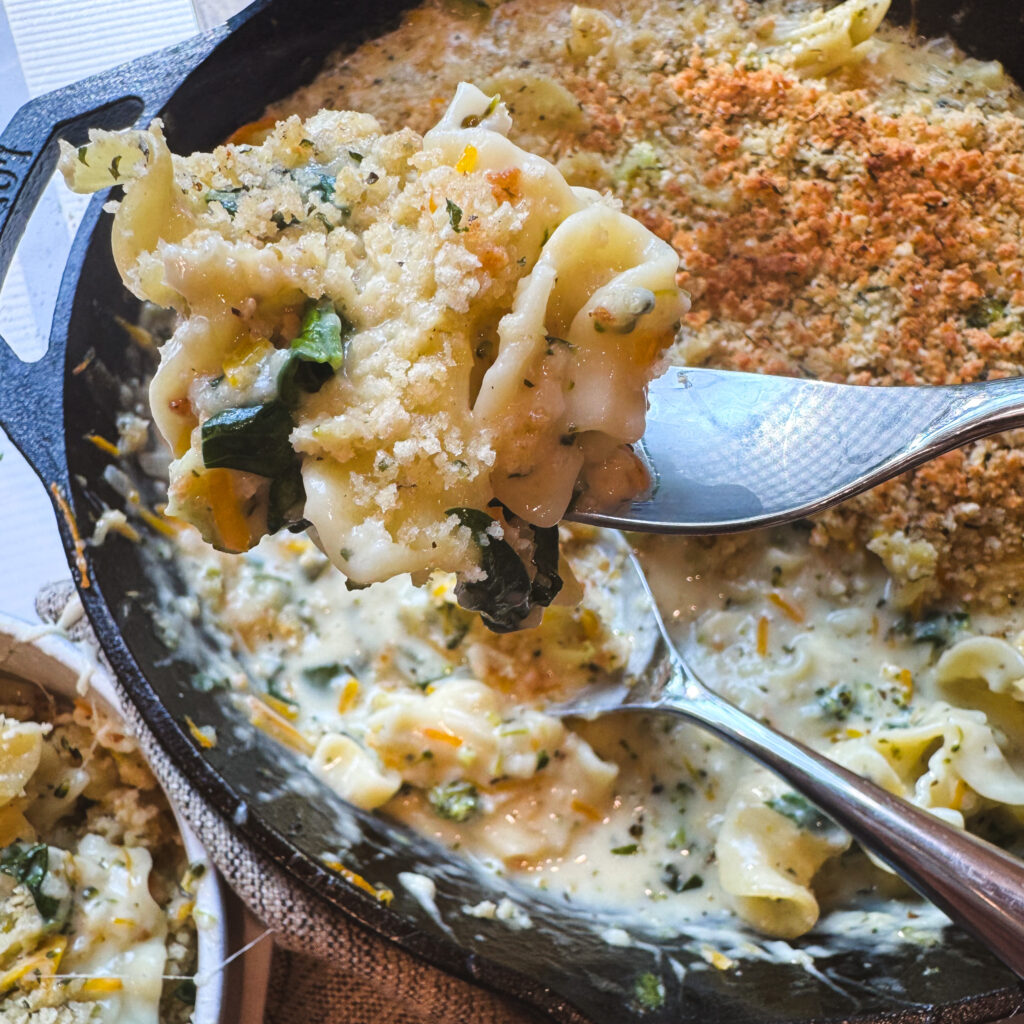 Spoonful of creamy white lasagna primavera with wide noodles, spinach and crispy breadcrumbs.