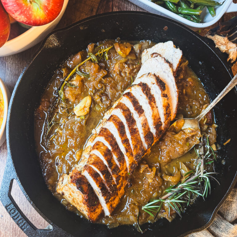 Sliced apple cider pork tenderloin served in a cast iron skillet with caramelized apples, onions and cider pan sauce.