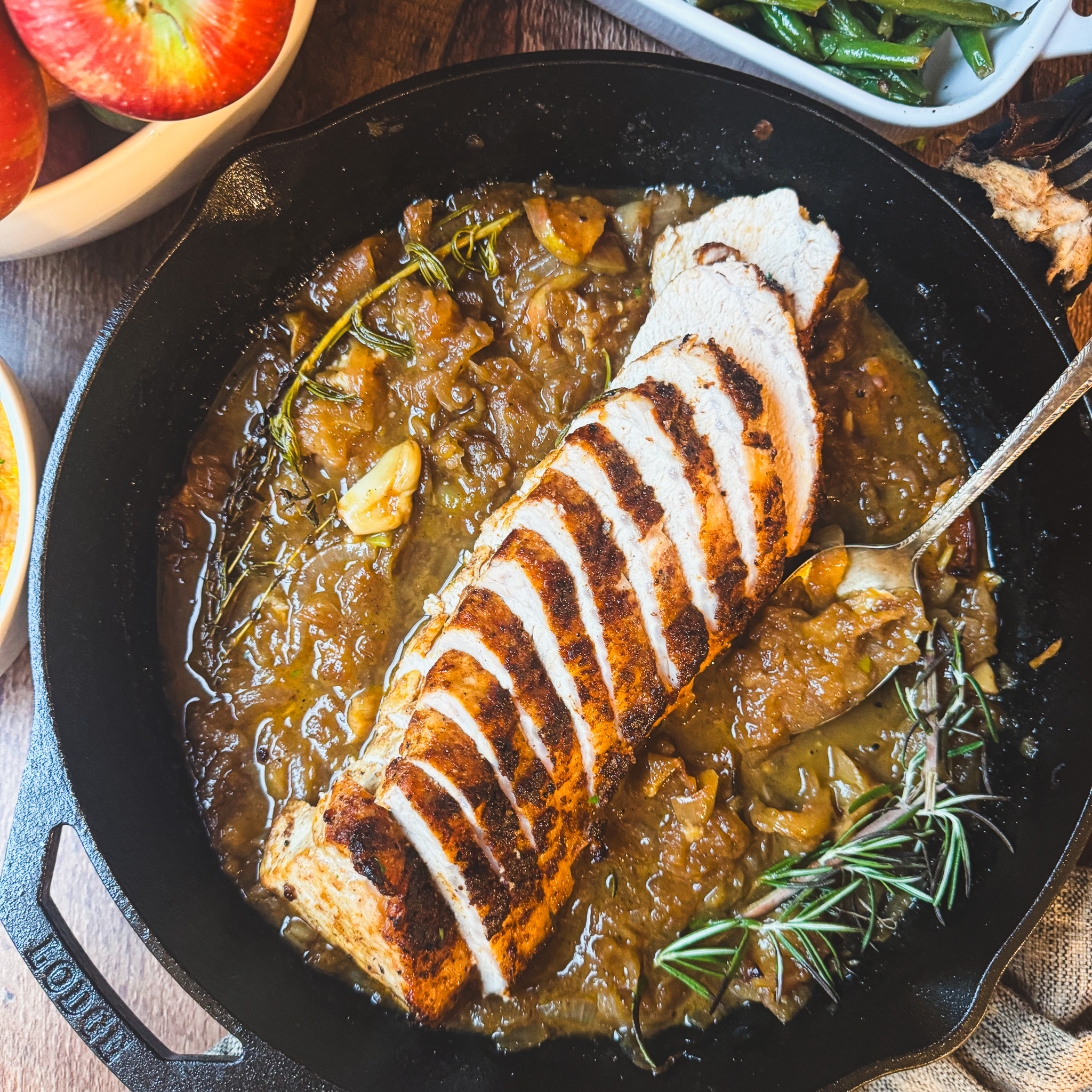 Sliced apple cider pork tenderloin served in a cast iron skillet with caramelized apples, onions and cider pan sauce.
