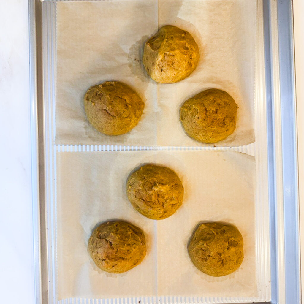 Freshly baked pumpkin whoopie pie cakes cooling on parchment-lined baking sheets before adding cream cheese filling.
