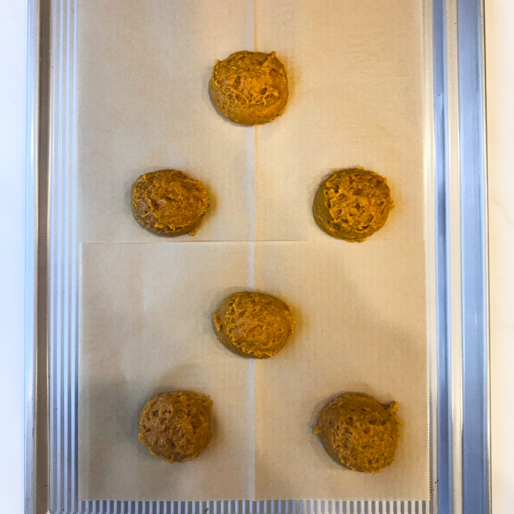 Scoops of pumpkin whoopie pie batter spaced apart on a parchment-lined baking sheet, ready to bake.