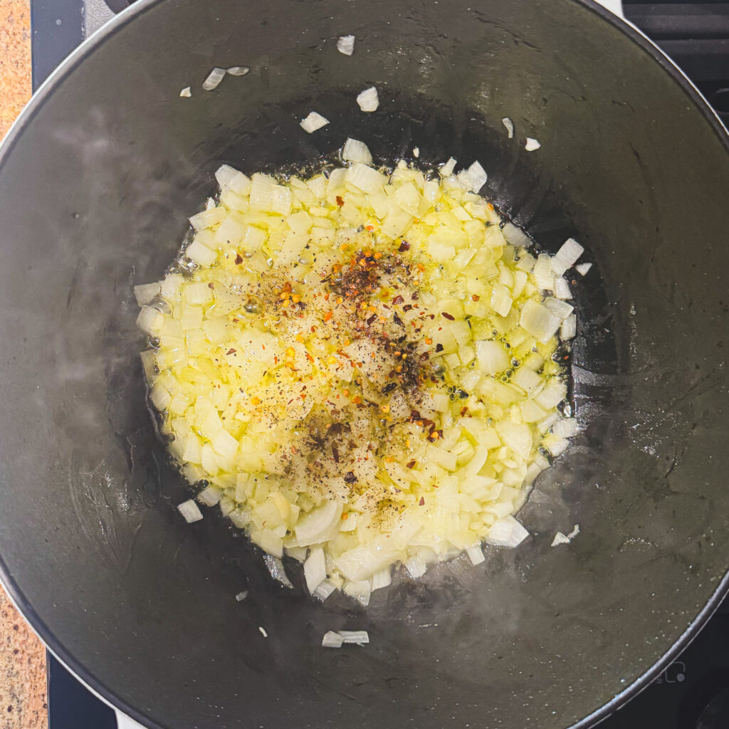 Diced onions, garlic, and seasonings sautéing in olive oil in a Dutch oven for homemade tomato cheddar soup.