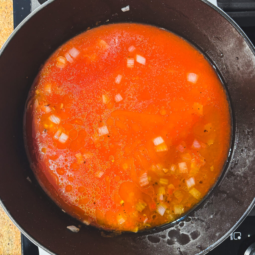 Adding tomatoes: Crushed San Marzano tomatoes and broth combined with sautéed onions and garlic in a Dutch oven.