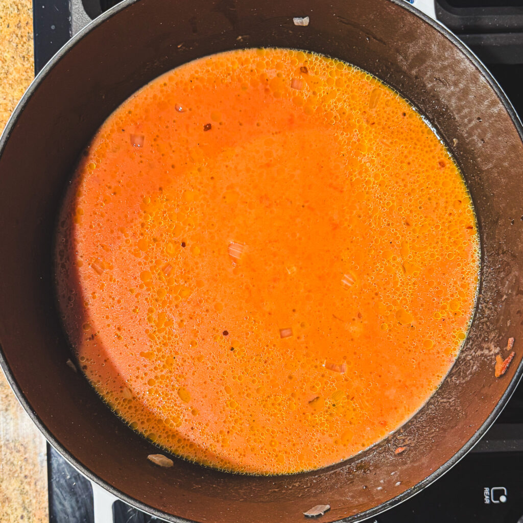 Adding cream: Tomato soup mixture with cream stirred into the crushed tomatoes and broth, creating a creamy orange-red base.