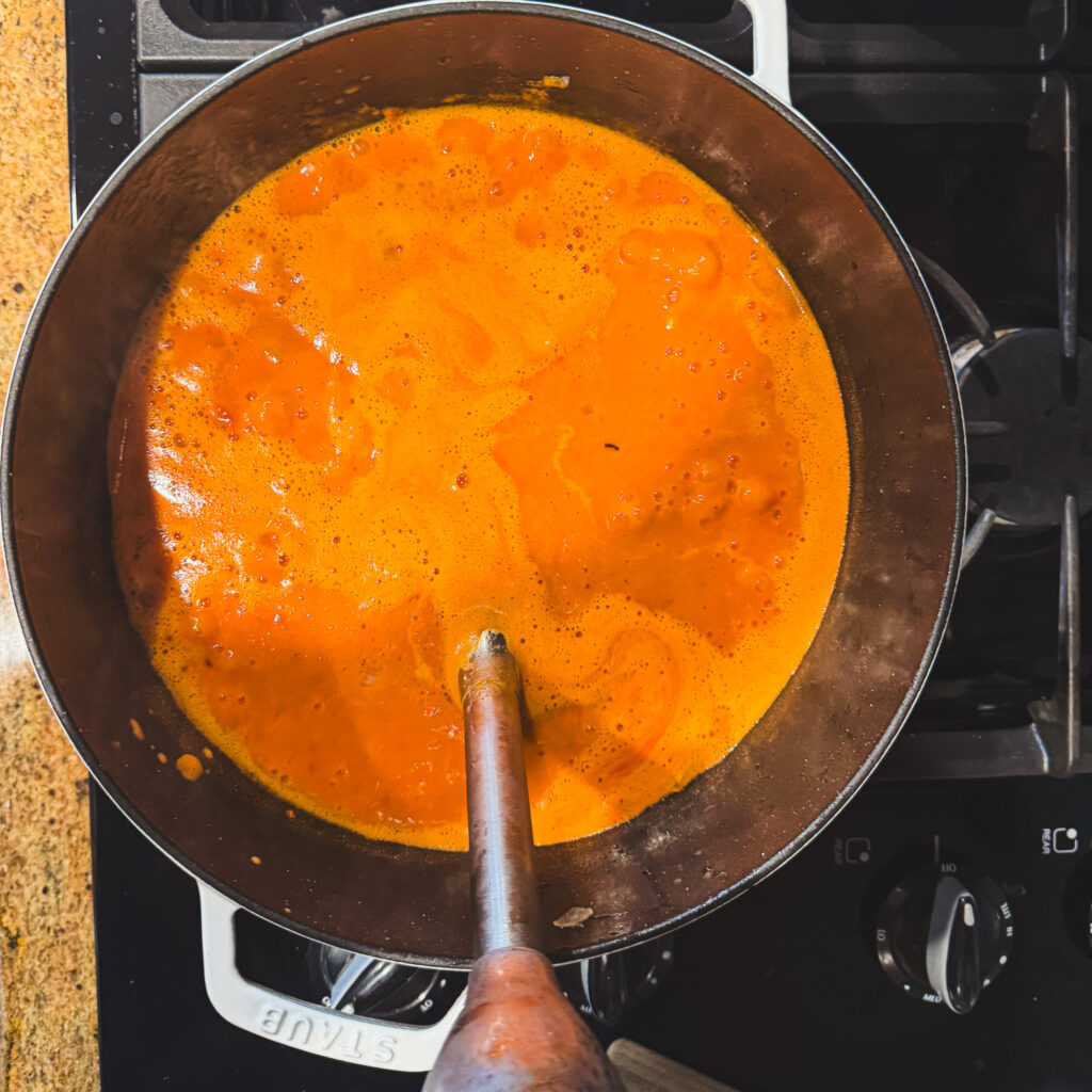 Blending soup: Creamy tomato soup being blended directly in a Dutch oven with an immersion blender until smooth.