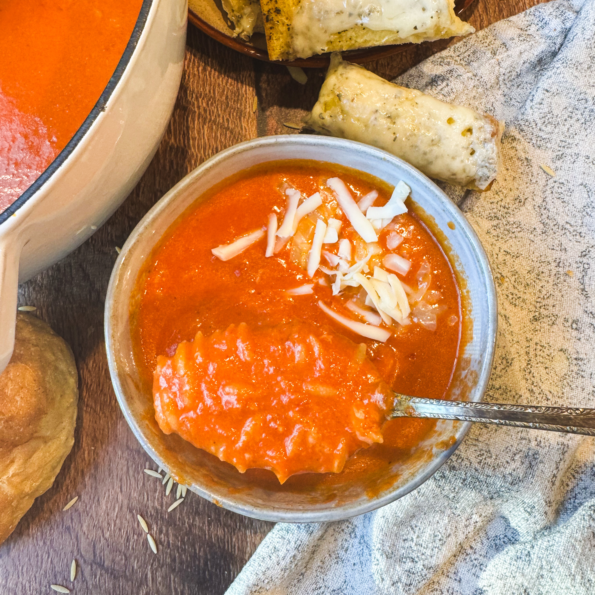 Spoonful of soup: Close-up of thick and creamy tomato cheddar orzo soup on a spoon, served with shredded cheddar cheese and crusty bread.
