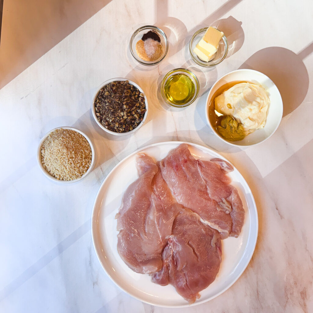 Overhead view of chicken cutlets, pecans, panko, mayonnaise, Dijon mustard, butter, olive oil, and seasonings.