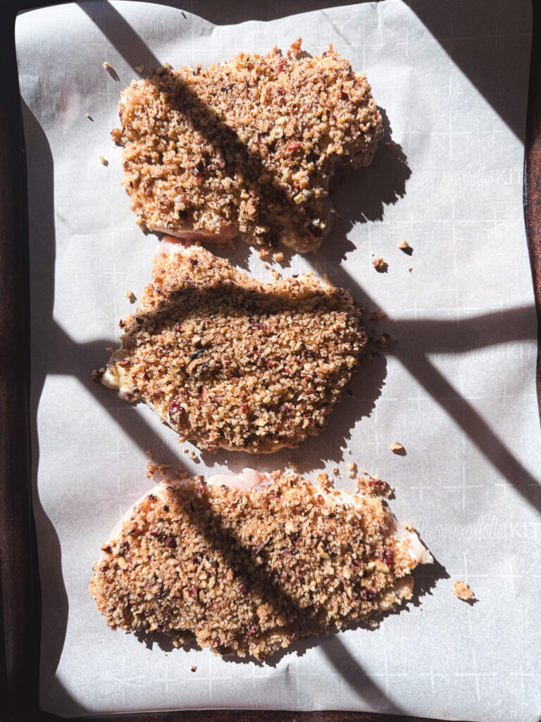 Unbaked pecan-crusted chicken cutlets arranged on a parchment-lined baking sheet.