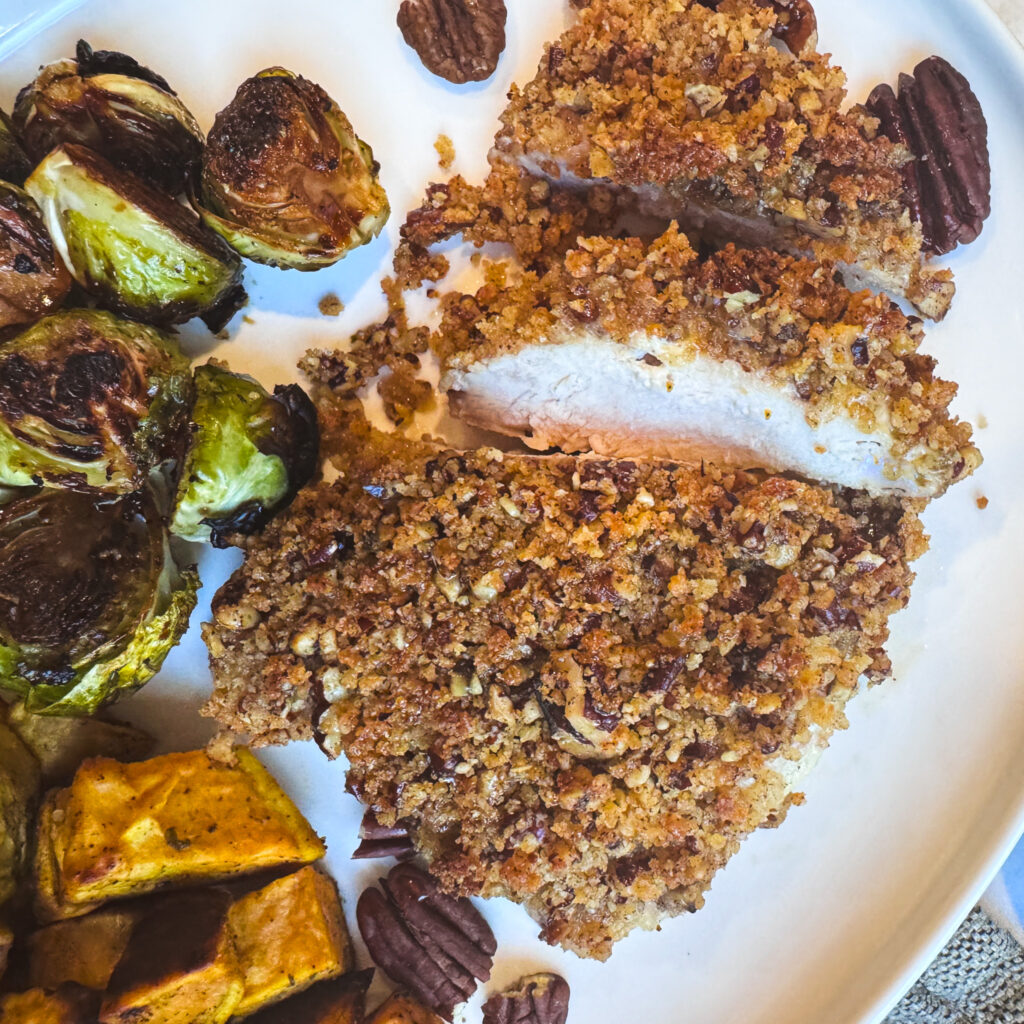 Close-up of juicy baked chicken cutlets covered in a golden pecan-panko crust.