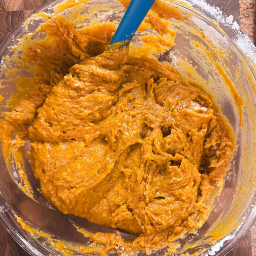 Thick orange pumpkin whoopie pie batter in a glass mixing bowl after combining the wet and dry ingredients.