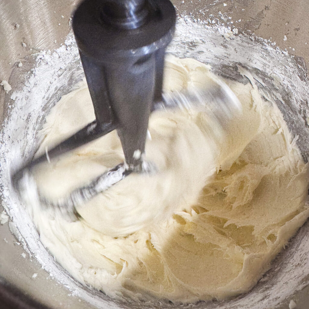Cream cheese buttercream being mixed with a paddle attachment until smooth and creamy for homemade pumpkin whoopie pies.