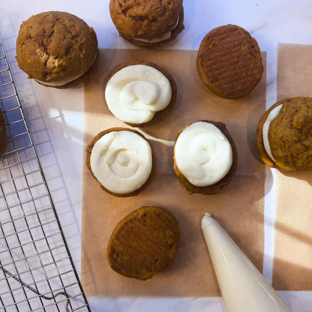 Thick cream cheese buttercream piped onto the flat sides of pumpkin whoopie pie cakes before sandwiching them together.